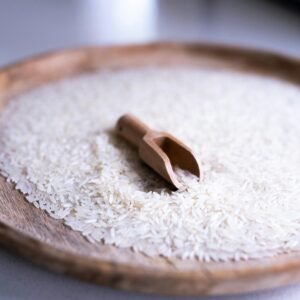 Minimalist image of uncooked white rice with a wooden scoop on a tray. Perfect for culinary themes.