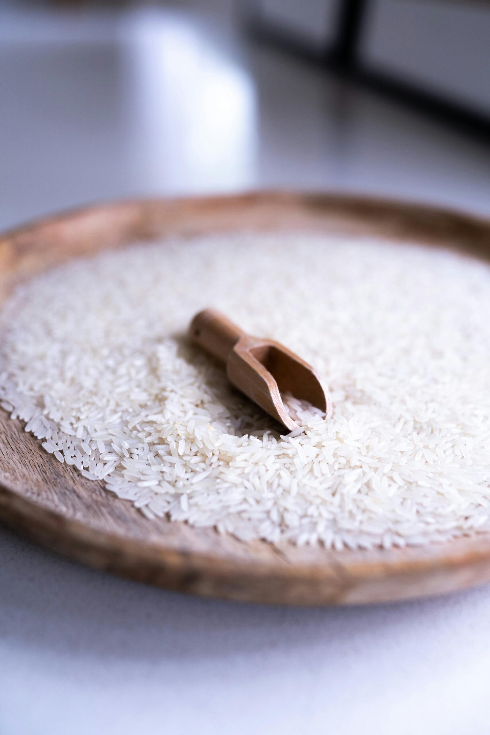 pexels photo 8251401 8251401 Minimalist image of uncooked white rice with a wooden scoop on a tray. Perfect for culinary themes.